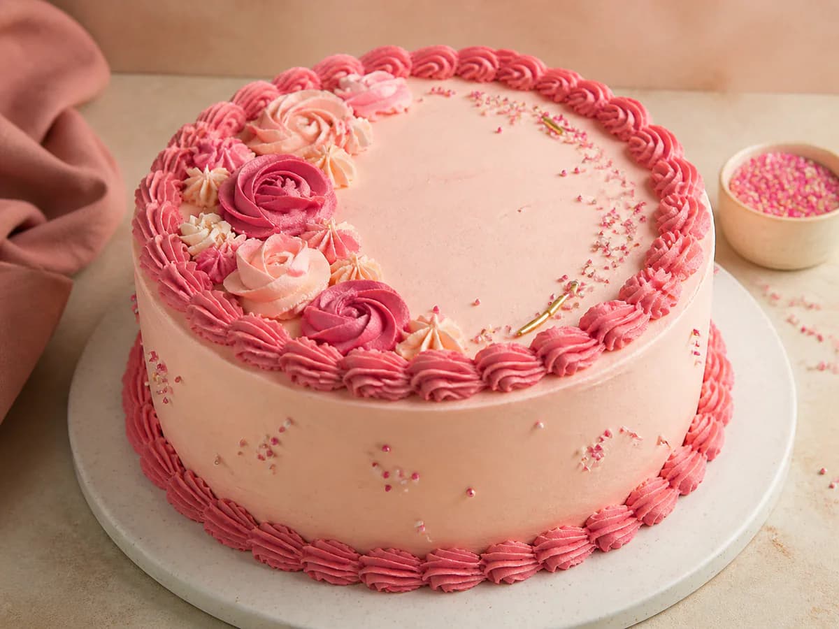 Pink buttercream birthday cake with piped rosettes and sprinkles